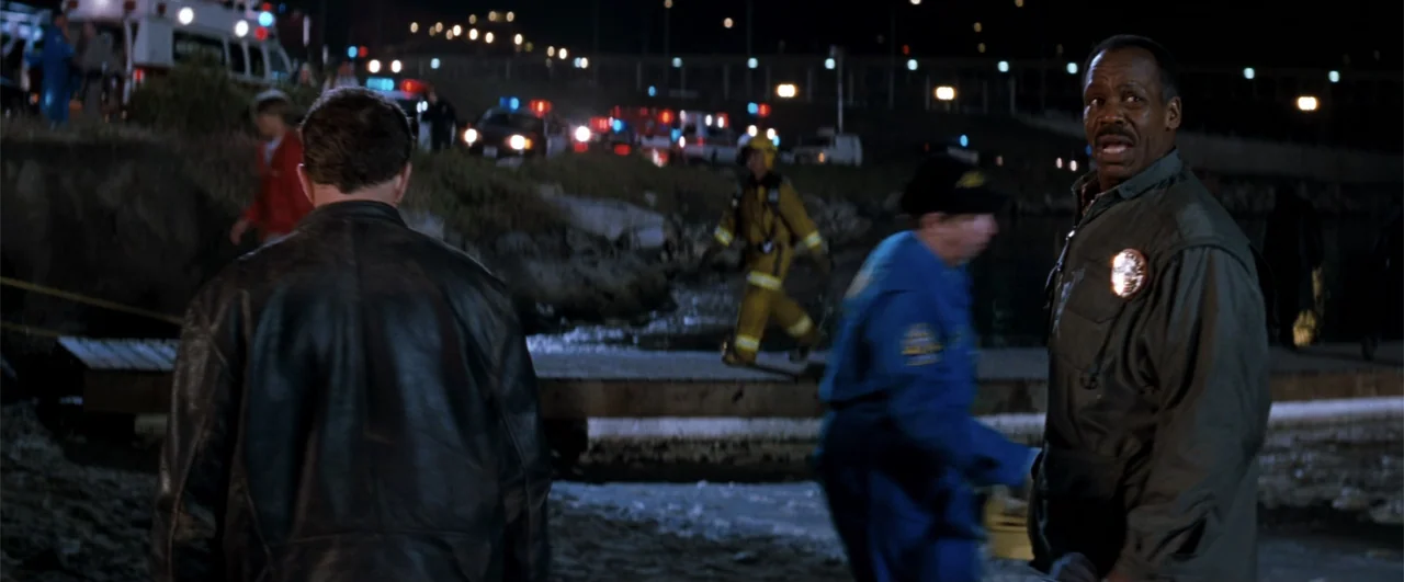 Lethal Weapon 4 (1998) movie still: medium — A night scene on a wooden dock with emergency vehicles and responders in the background. A police…