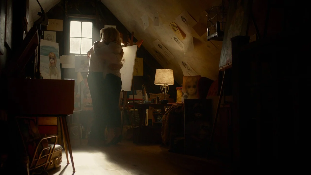 Big Eyes (2014) movie still: fullbody — An attic space with sloped walls contains many paintings and scattered drawings on walls. A man and a woman…