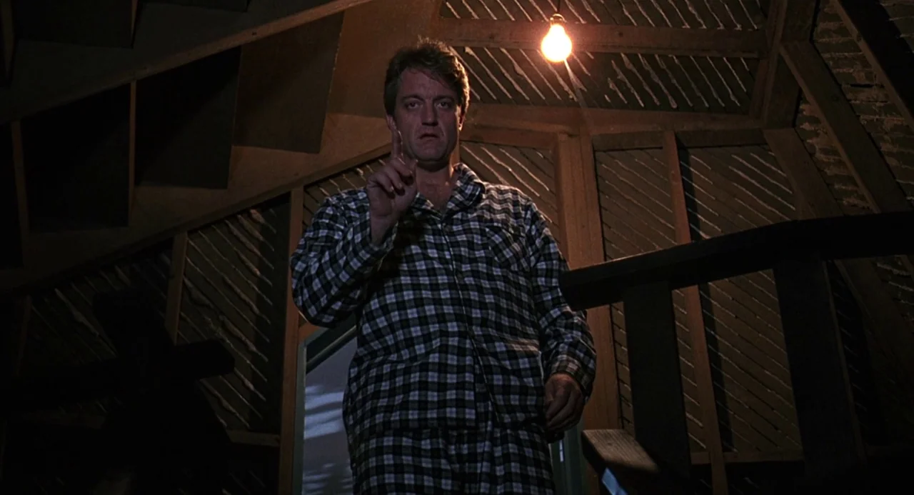 Child’s Play 2 (1990) movie still: medium — A dark, unfinished wooden attic interior with exposed beams and shadow-filled corners. A man in plaid…