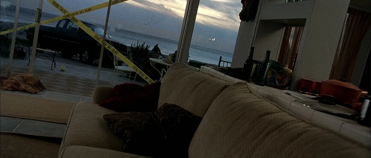 A Man Apart (2003) movie still: medium — A living room interior faces a large glass window overlooking a beach at dusk. Yellow police caution tape…