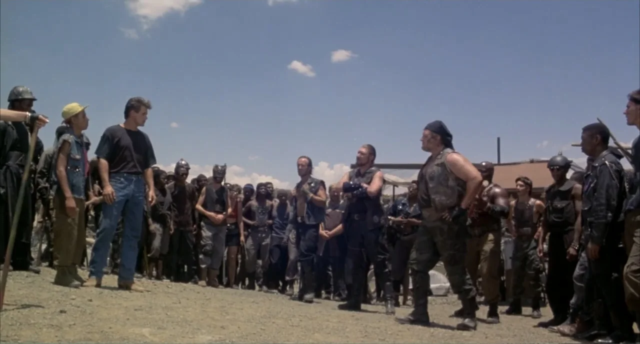 American Ninja 4: The Annihilation (1990) movie still: wide — A desolate, gravel-covered clearing under a clear blue sky. A man in jeans and a…