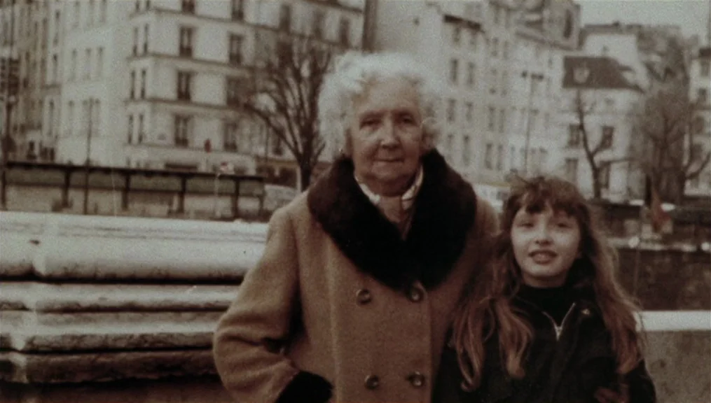 Before Sunset (2004) movie still: medium — An elderly woman and a girl stand on a bridge with multi-story buildings visible behind. The subjects…