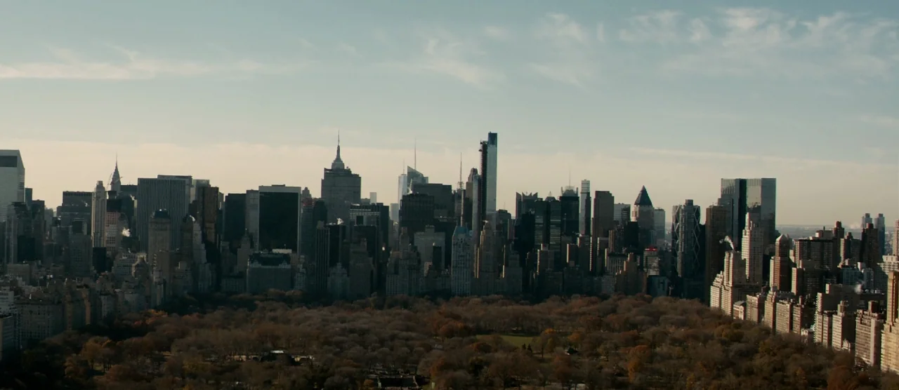 Self/less (2015) movie still: establishing — A dense metropolitan skyline rises above a large, leafless park in late autumn. Numerous skyscrapers of…
