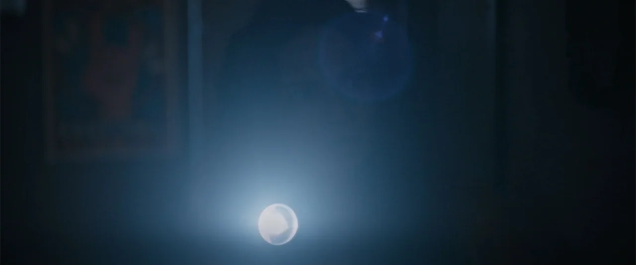 Silent Night, Deadly Night (2025) movie still: closeup — A very dark interior space shows only the source of a concentrated beam of light. A person…