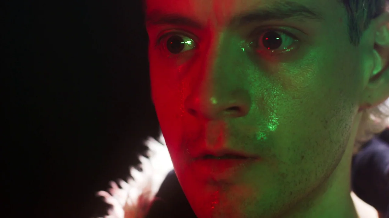 Carnage for Christmas (2024) movie still: closeup — A close-up of a young man's face illuminated by contrasting red and green light. The subject…