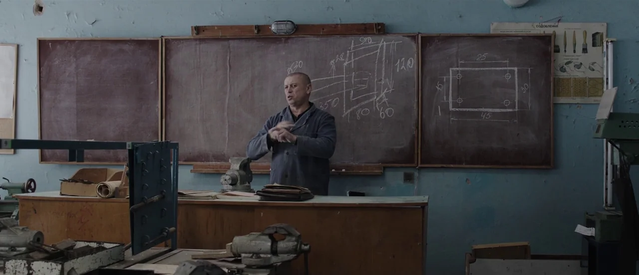 The Tribe (2014) movie still: medium — A workshop room features light blue walls and large dark chalkboards covered in technical diagrams. A…