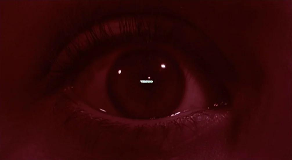 Vertigo (1958) movie still: closeup — A dark red-tinted close-up shows a single human eye looking directly forward. The word Vertigo appears as a…