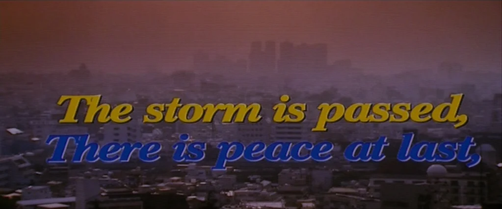 The Brothers Bloom (2008) movie still: establishing — A wide view of a dense urban skyline under a hazy twilight sky. Overlaid text appears in the…