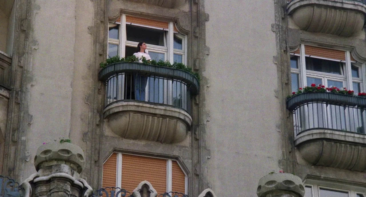 Etoile (1989) movie still: wide — A multi-story stone apartment building features several small arched balconies with iron railings. A young woman…