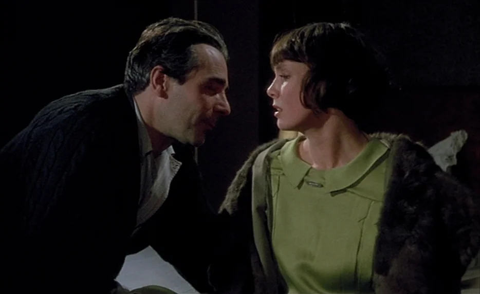 Mélo (1986) movie still: medium — A dark, minimally lit space provides a backdrop for two people in conversation. A man leans toward a woman who is…