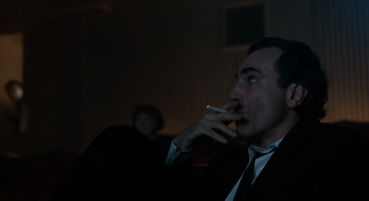 The Great Beauty (2013) movie still: medium — A dark movie theater with rows of empty seats dimly visible in the background. A man in a suit sits in…
