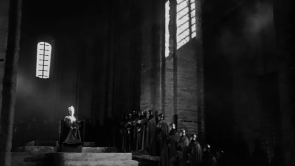 Falstaff (Chimes at Midnight) (1965) movie still: wide — A dark stone interior of a medieval structure features tall windows with light shafts. A…