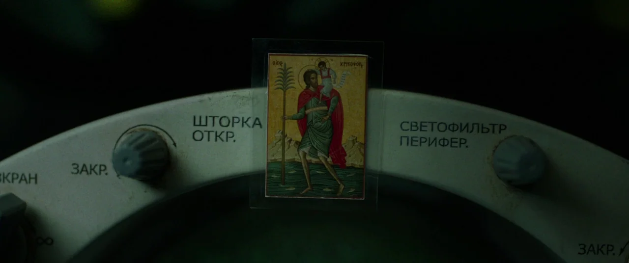 Gravity (2013) movie still: closeup — A curved white metal control panel with Cyrillic text features two adjustment knobs. A small religious icon is…
