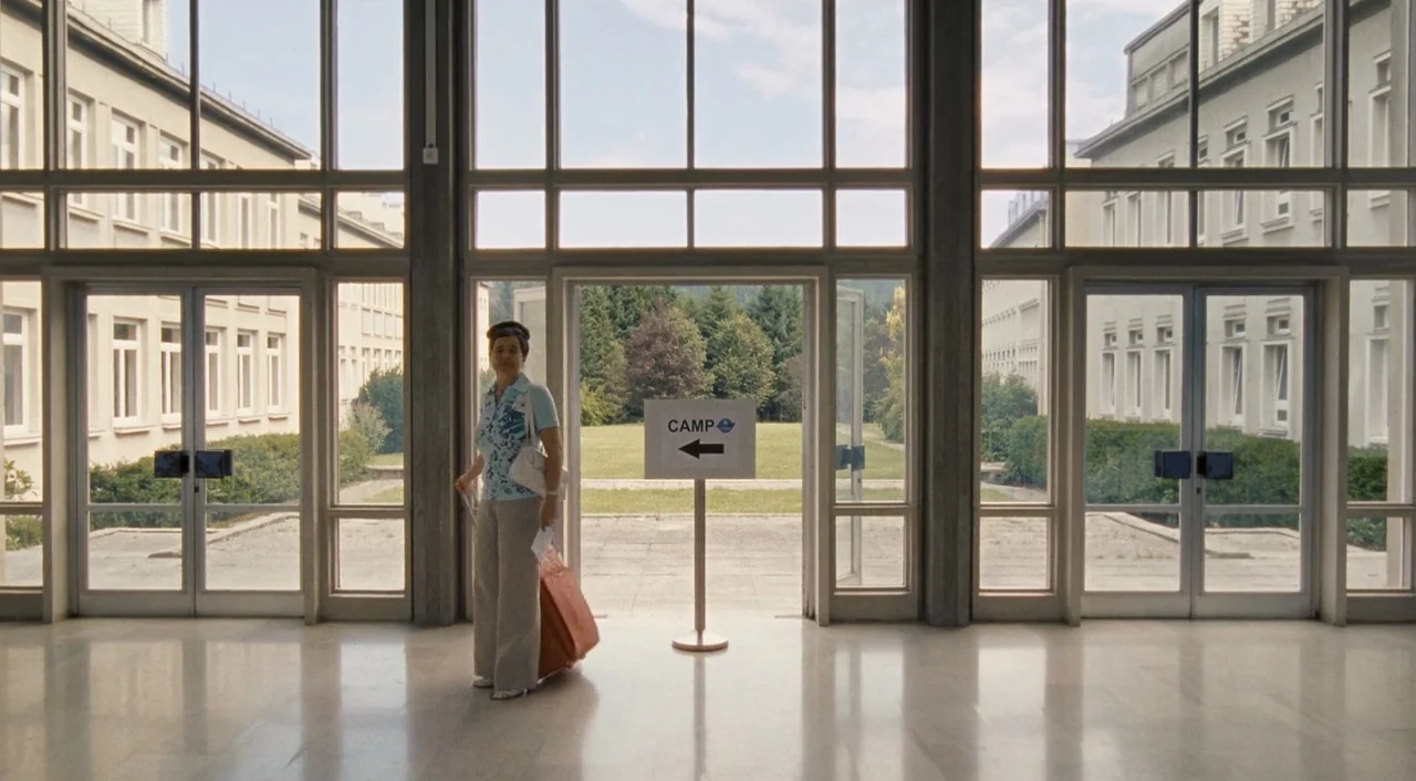 Paradise: Hope (2013) movie still: fullbody — A spacious, minimalist lobby features white marble floors and extensive glass window panels. A woman…