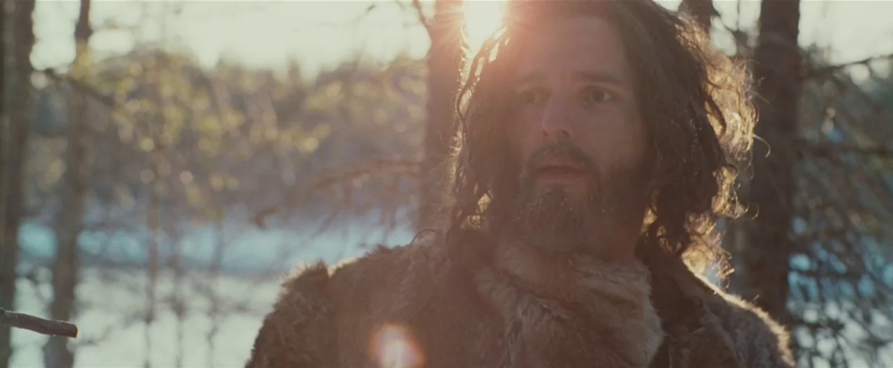 Hanna (2011) movie still: medium — A dense woodland with thin, bare trees and patches of snow on the ground. A man with a thick beard and fur coat…