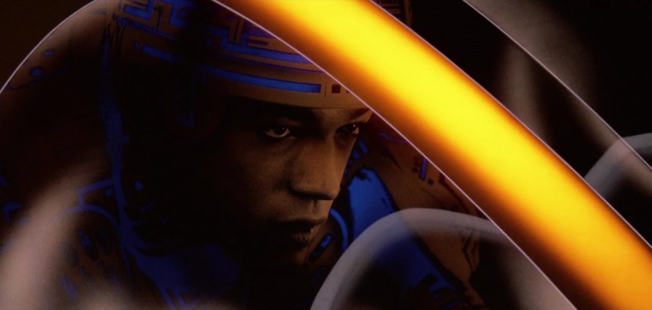 Tron (1982) movie still: closeup — A close view of a man inside a futuristic, sleek light cycle. Blue circuitry patterns decorate his suit and…