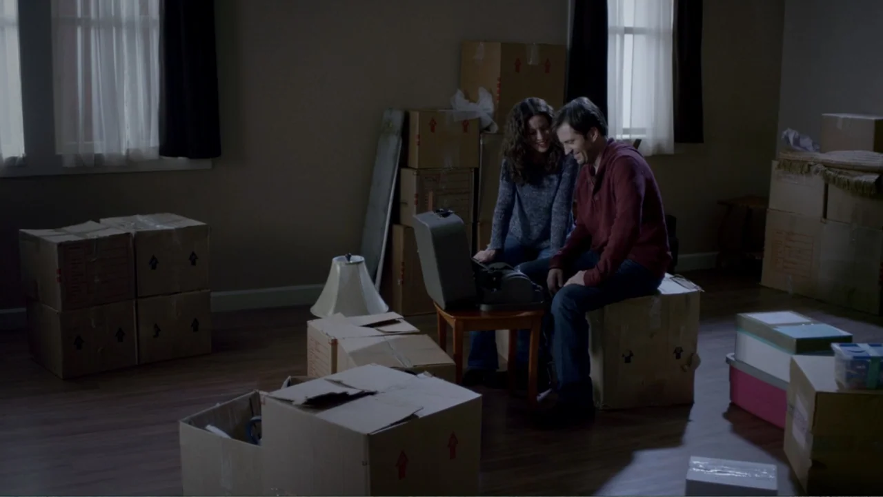 It's Christmas, Carol! (2012) movie still: medium — An unfurnished room contains numerous stacked cardboard moving boxes placed across the hardwood…