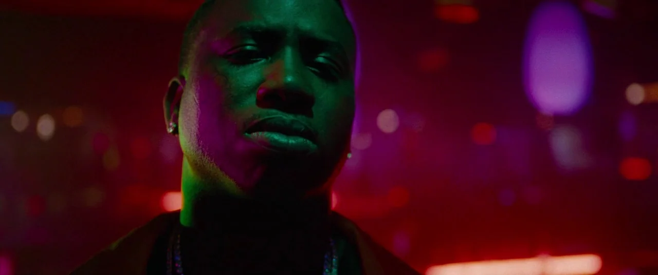 Spring Breakers (2012) movie still: closeup — A dimly lit club interior with blurred colorful bokeh lights in the background. A man stands in the…