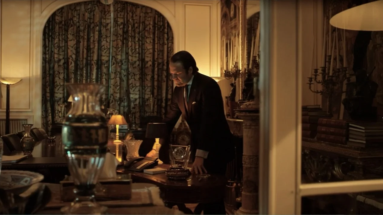 Entre las sombras (2025) movie still: medium — A luxuriously decorated room features dark wood furniture, ornate curtains, and several small lamps.…