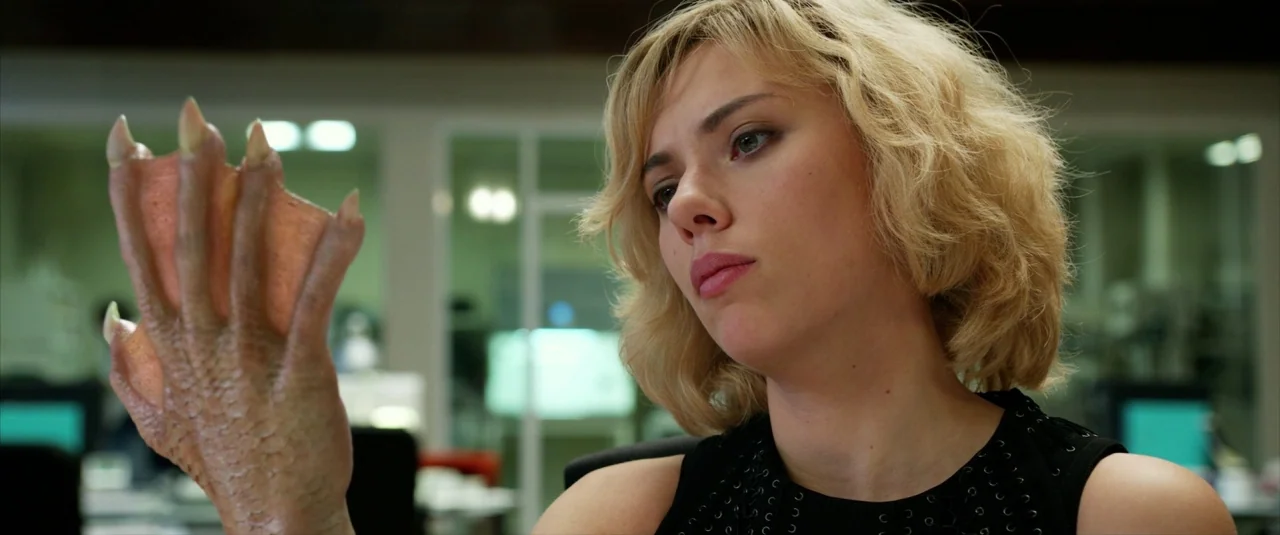 Lucy (2014) movie still: medium — A sterile laboratory setting features bright white walls and blurred glass partitions. A woman examines a…