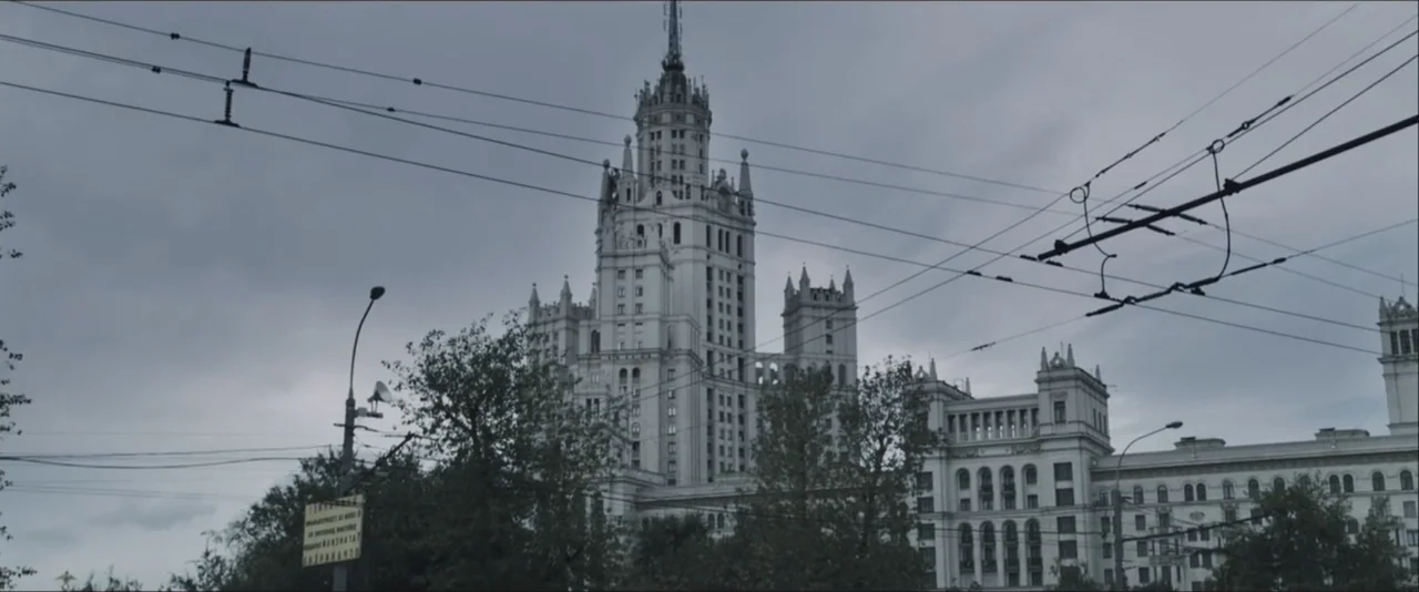 Darkest Hour (2017) movie still: establishing — A massive Stalinist skyscraper stands against a dense, overcast grey sky. Overhead power lines…