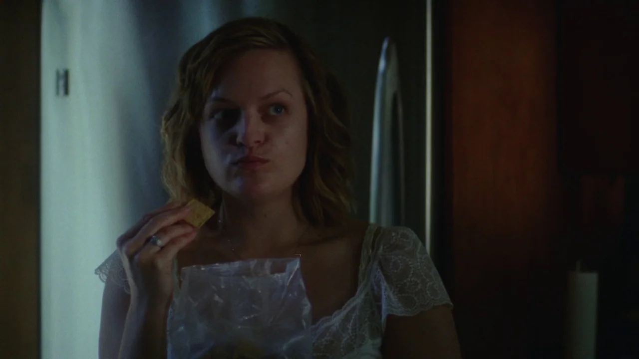 Queen of Earth (2015) movie still: closeup — A dark, dimly lit indoor setting features a person standing in a home environment. The woman holds a…