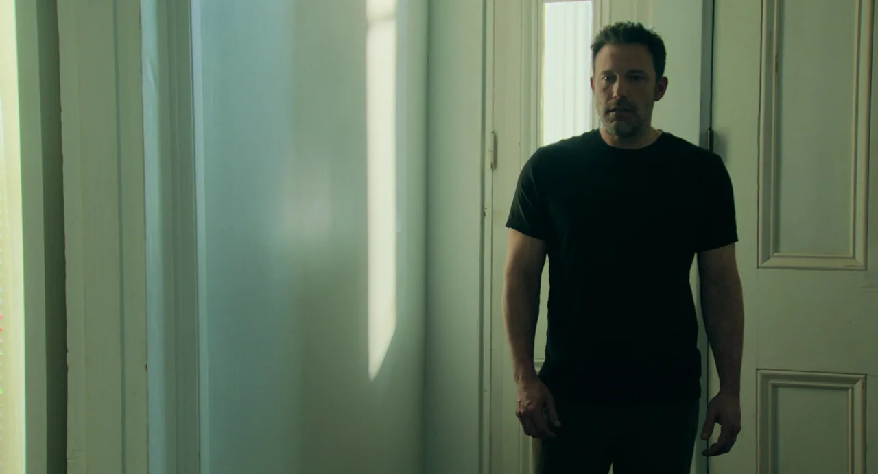 Deep Water (2022) movie still: medium — A spare, neutral-toned interior hallway features pale blue-grey walls and white door frames. A man in a…