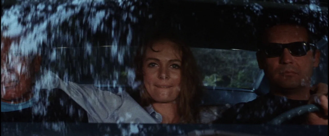 Point Blank (1967) movie still: medium — Three people sit side-by-side in the front seat of a car. The view is seen through the windshield, with…