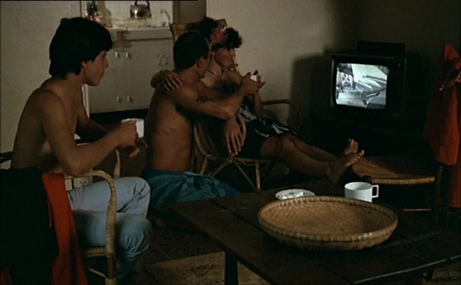 Pauline At the Beach (Pauline à la plage) (1983) movie still: medium — A dimly lit room contains three people sitting near a television set. A…