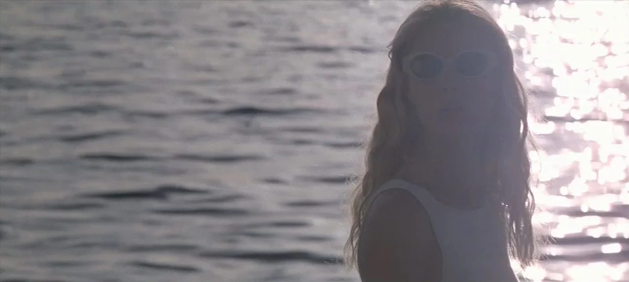 Great Expectations (1998) movie still: medium — A woman stands in front of a body of water during the day. The sunlight reflects intensely off the…