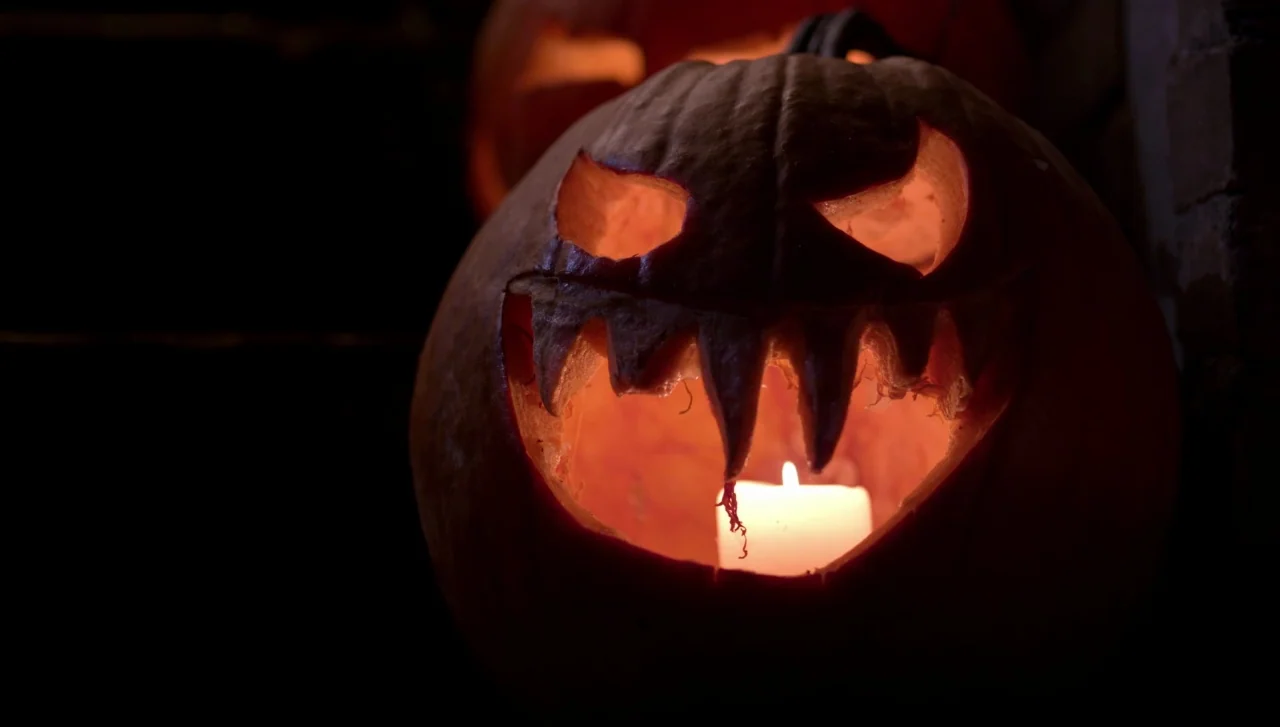 Hellions (2015) movie still: closeup — A carved pumpkin sits in darkness with an internal candle illuminating its jagged features. The hollow…