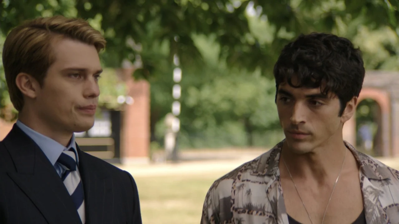 Red, White & Royal Blue (2023) movie still: medium — A green park setting with blurred trees and brick structures in the background. Two men engage…