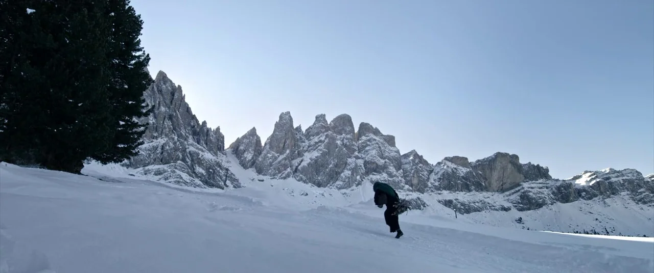 A Hidden Life (2019) movie still: wide — A expansive snow-covered mountain slope is set against a backdrop of jagged, rocky peaks. A person wearing…