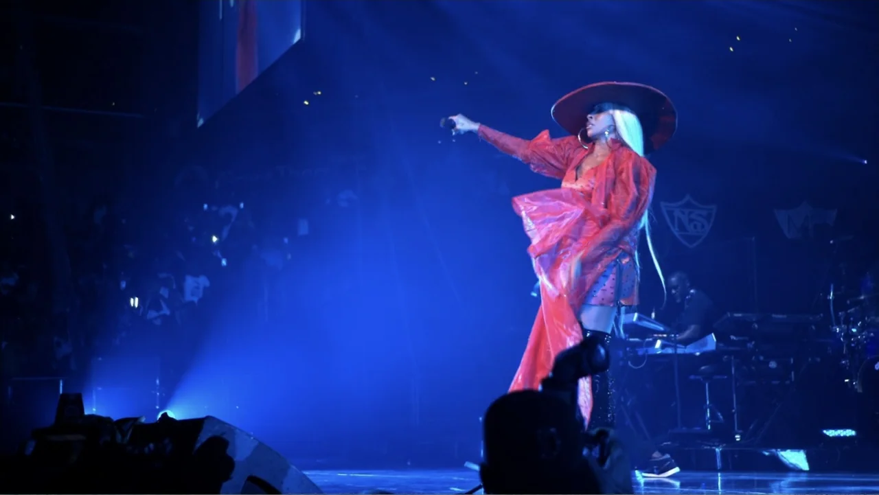 Mary J. Blige's My Life (2021) movie still: fullbody — A performer stands on a large dark stage under intense blue spotlight beams. The artist wears…