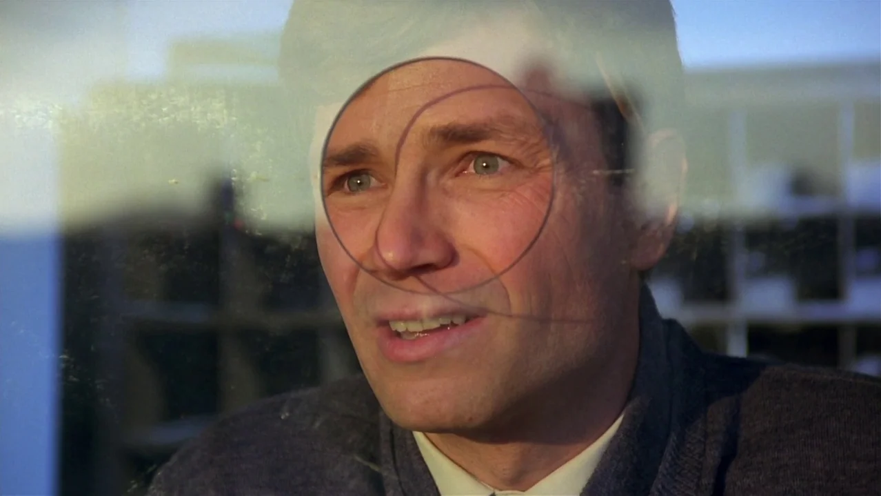 Pee-Wee’s Big Adventure (1985) movie still: closeup — A man looks through a circular wiped section of a smudged train window. He sits inside a…