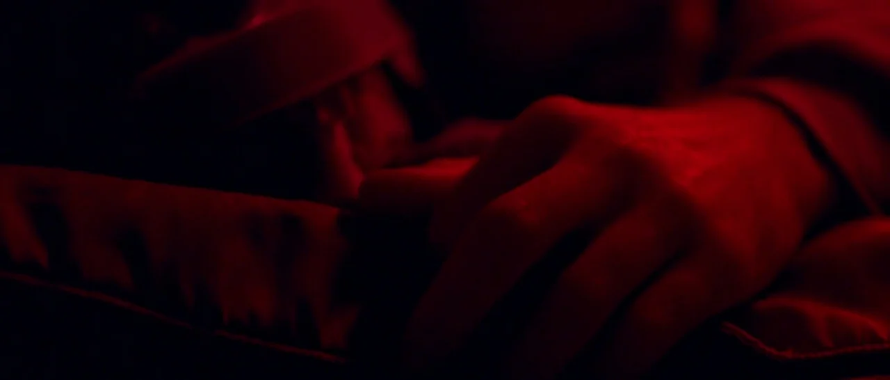 Good Time (2017) movie still: closeup — A dark, indistinct space is illuminated by a deep red light source. A person's hand rests palm down upon a…