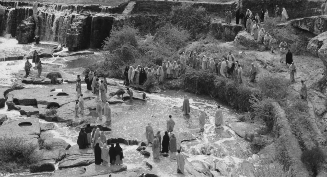 The Gospel According To St. Matthew (1964) movie still: establishing — A rocky riverbed features a large waterfall spilling into a tiered pool…