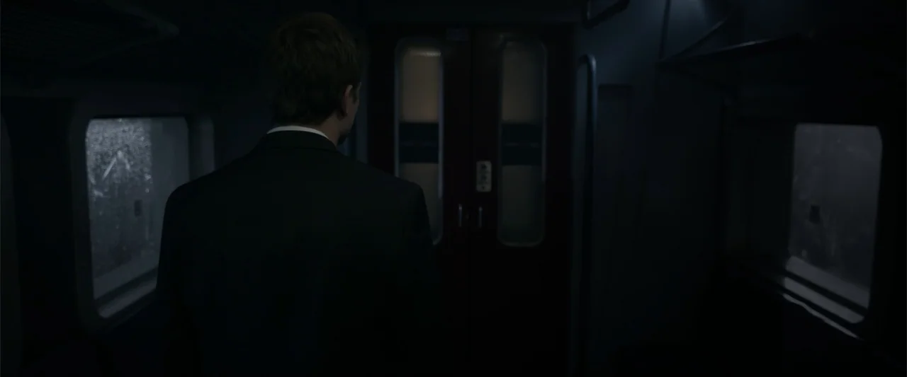 Howl (2015) movie still: medium — A dimly lit train carriage interior features rain-streaked windows and a central sliding door. A man in a dark…