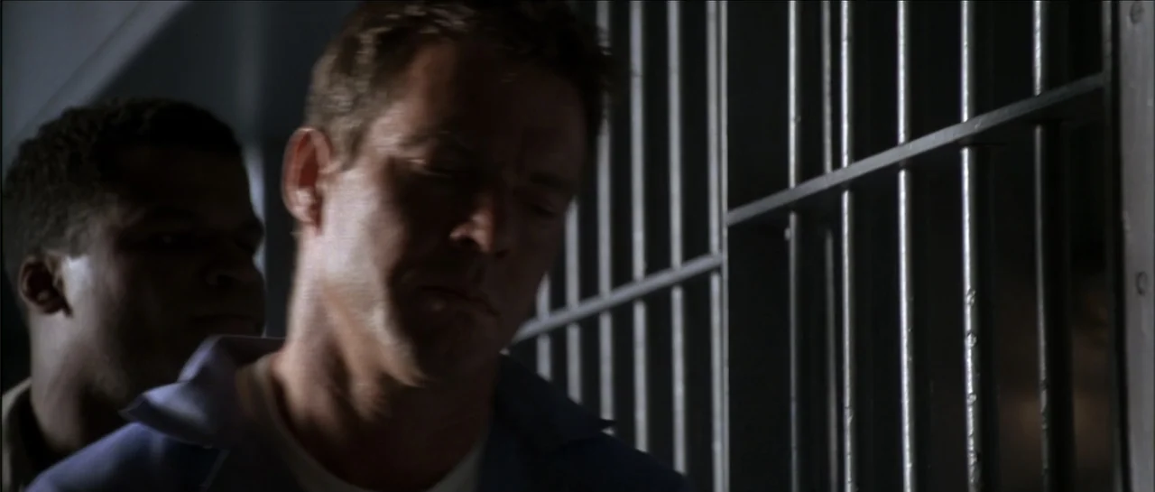 Gang Related (1997) movie still: medium — A dimly lit room features heavy vertical metal bars in the background. Two men stand in close proximity…