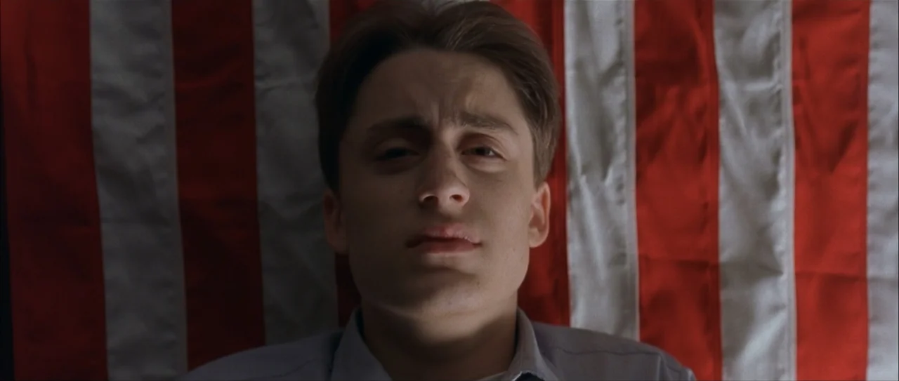 Igby Goes Down (2002) movie still: closeup — A man is positioned directly in front of a red and white striped fabric backdrop. The subject lies…