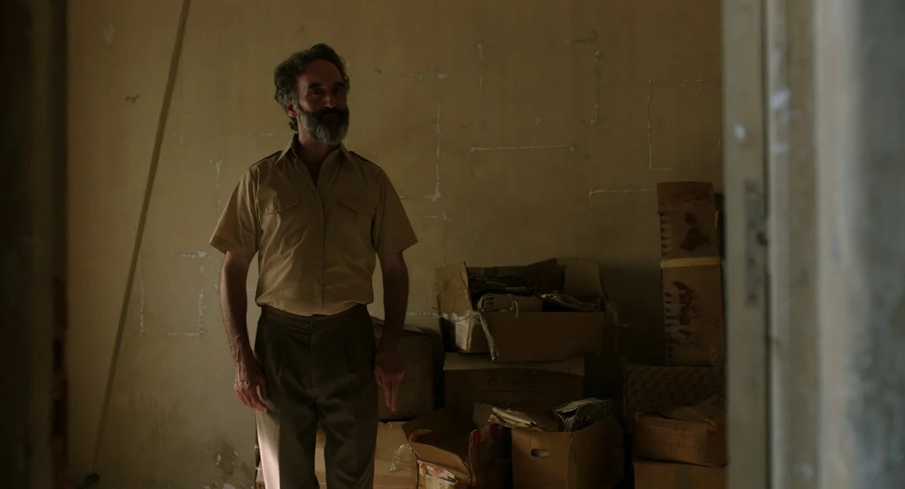 Crimes of the Future (2022) movie still: fullbody — A sparsely furnished storage room contains stacks of aged cardboard boxes against a wall. A man…