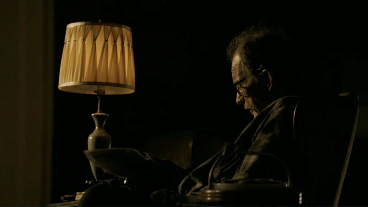 The Texas Chainsaw Massacre: The Beginning (2006) movie still: medium — A dark living room contains a single lit lamp next to a chair. An older man…