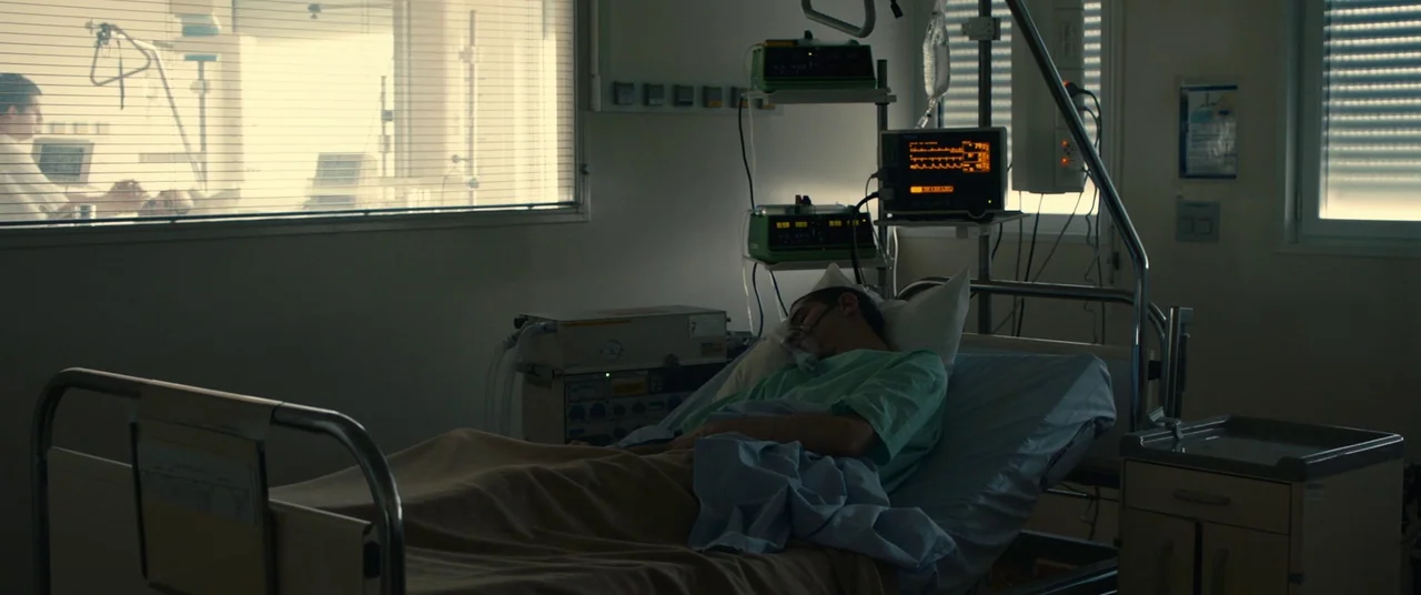 BPM (Beats Per Minute) (2017) movie still: wide — A hospital room contains medical machinery and a patient lying on a metal frame bed. A second…