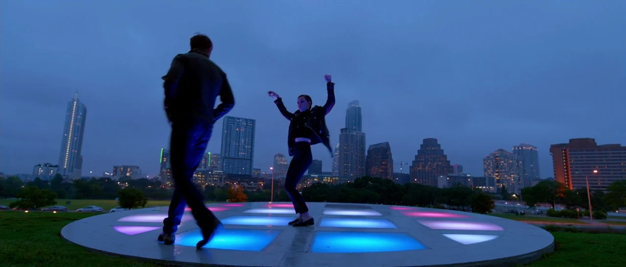 Song to Song (2017) movie still: wide — An elevated circular platform with glowing floor tiles sits in a public city park. A man and a woman perform…