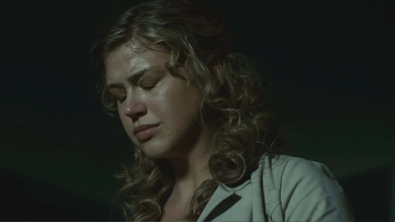 Legion (2010) movie still: closeup — A dark indoor space with minimal visible detail beyond the subject. A young woman with blonde hair stands with…