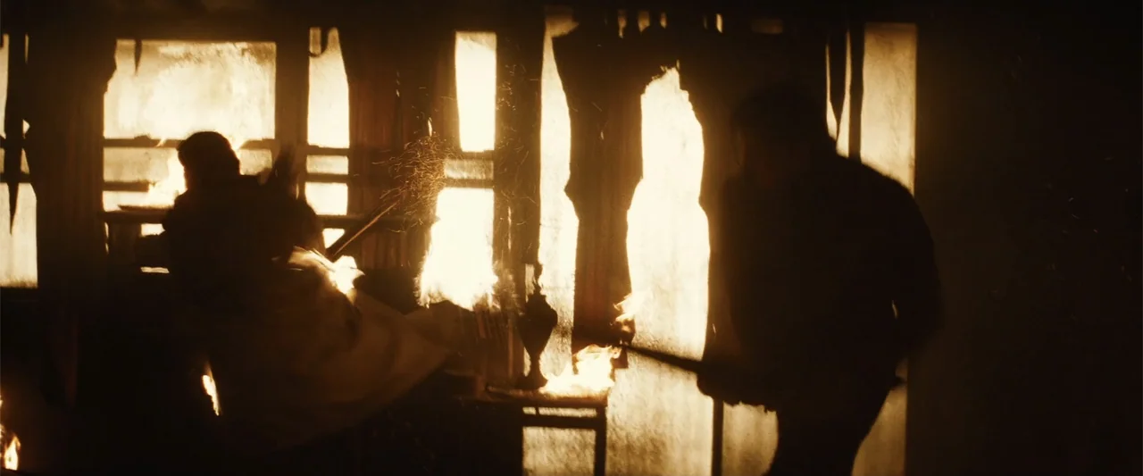Run All Night (2015) movie still: medium — A dark interior space is illuminated by bright flames consuming objects near windows. Two figures stand…