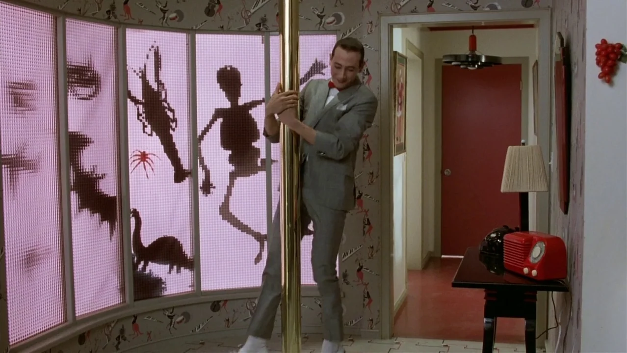 Pee-Wee’s Big Adventure (1985) movie still: fullbody — A whimsical hallway features patterned wallpaper with cartoonish motifs and translucent pink…