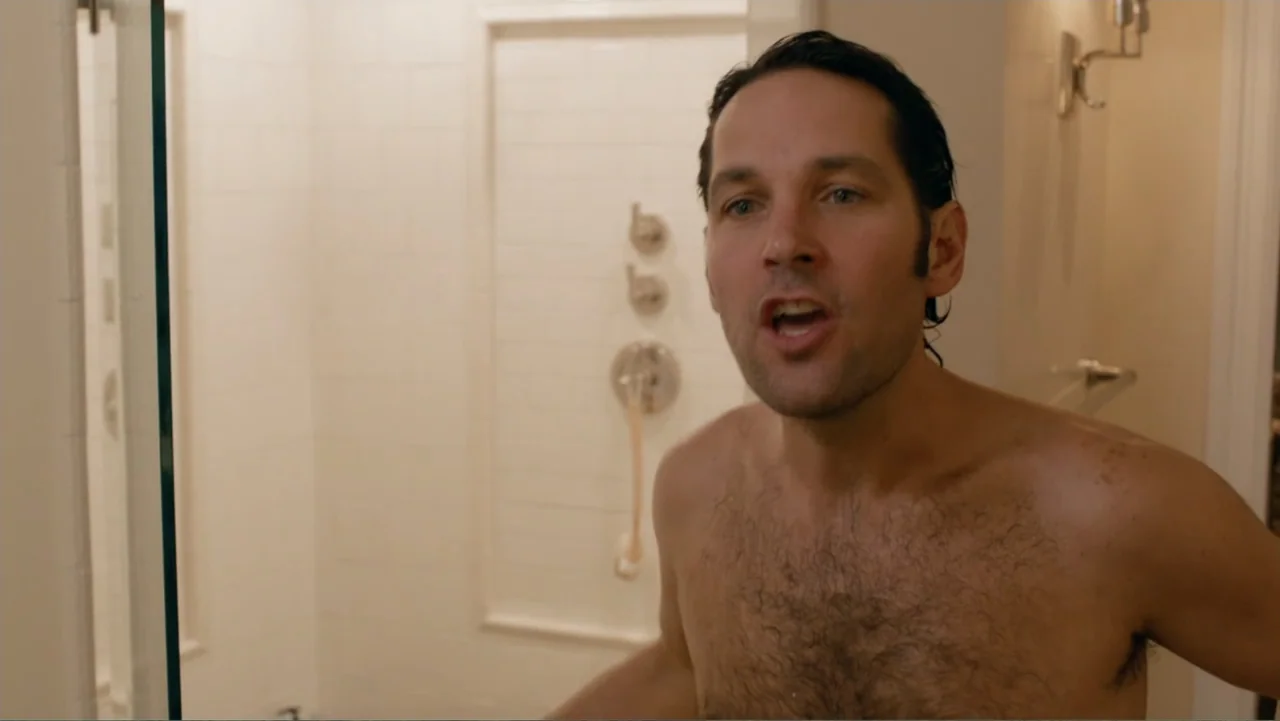 This Is 40 (2012) movie still: medium — A modern bathroom features light-colored square tile walls and recessed shower fixtures. A man with dark…