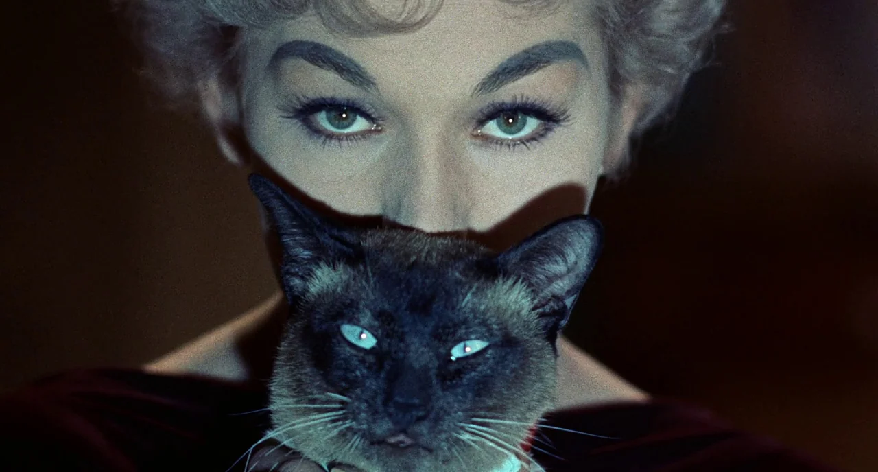 Bell Book and Candle (1958) movie still: closeup — A dark, underexposed indoor space provides a stark backdrop for a woman's face. She holds a…