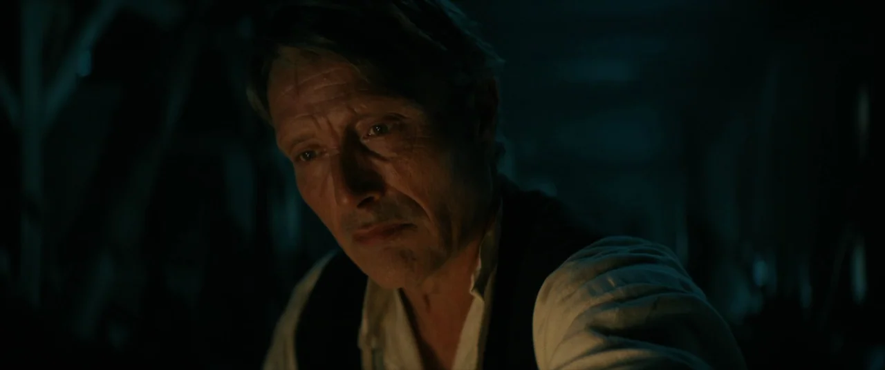 The Promised Land (2023) movie still: closeup — A dark, dimly lit space with soft shadows obscuring the surrounding environment. An older man gazes…